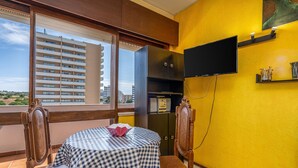 Ein Balkon mit einem karierten Tisch, Stühlen, einem an der Wand befestigten Fernseher und Blick auf ein Gebäude.