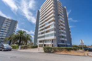 Un edificio residencial de varios pisos con balcones, una señal de estacionamiento y palmeras.