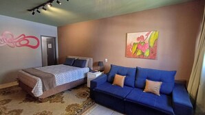 A bedroom with a bed, a blue sofa, a rug, a painting, and a door. - Studio Barreto Leme 72 (Campinas)