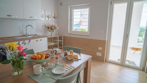 Une cuisine avec un coin repas, une fenêtre donnant sur un beau paysage et un chien à l’extérieur.