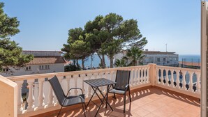 Un balcone con due sedie e un tavolo, con vista su una zona costiera con edifici e alberi.