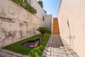 A narrow courtyard with a small water feature, a potted plant, and a staircase.