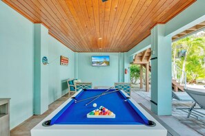 A pool table with a blue felt surface, surrounded by light green walls and wooden ceiling beams.