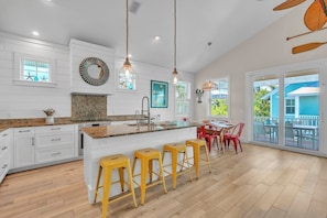 A spacious kitchen with a large island, wooden bar stools, and a dining area with red chairs.