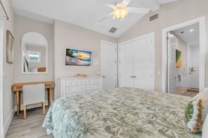 A bedroom with a bed, a desk, a dresser, a ceiling fan, and a painting on the wall.
