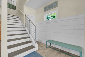 A staircase with a metal railing, a bench, a window with a star decoration, and a wall sign that reads 'BEACH'.