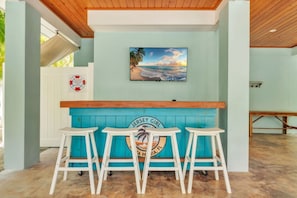A bar area with a blue wall, a painting of a beach, and three stools.