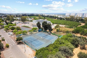 Una cancha de tenis rodeada de vegetación y edificios.