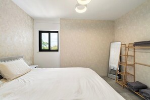 A bedroom with a bed, a window, a mirror, and a wooden shelf with towels.