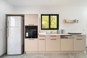 Een moderne keuken met een inbouwoven, een koelkast en een raam met uitzicht op bomen.