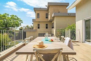 Una terrazza con un tavolo apparecchiato per due, una piscina sullo sfondo e un edificio a più piani.