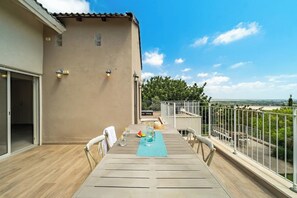 Ein Balkon mit Esstisch, Blick auf die Landschaft und ein Gebäude mit beige gefärbter Fassade.