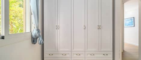 A white wardrobe with multiple drawers and doors, positioned next to a window with a curtain.