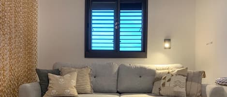 A neutral-toned sofa with patterned cushions, a woven rug, and a window with blinds.
