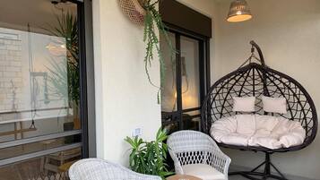 A balcony with wicker furniture, a hanging chair, and potted plants.