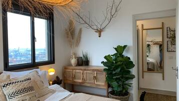 Un dormitorio con una cama, un ventanal grande, una cabeza de venado montada en la pared, una planta en maceta y un armario de madera.