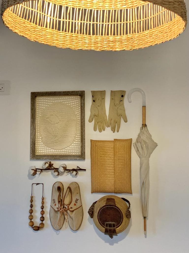 Una parete con diversi oggetti, tra cui una lampada intrecciata, un'opera d'arte incorniciata, guanti, un ombrello, un libro, un paio di scarpe, una collana di perline e un cappello.