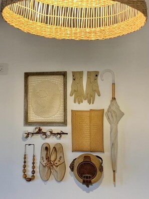 A wall with various items including a woven light fixture, a framed artwork, gloves, an umbrella, a book, a pair of shoes, a beaded necklace, and a hat. - Boho Chic 2BR • Rooftop • Mamad by SeaNRent (Tiberias)