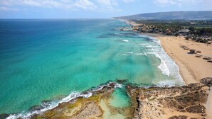 Paesaggio costiero con spiaggia, acque turchesi limpide e un litorale roccioso.