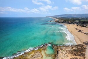 Un paysage côtier avec une plage, des eaux turquoise et limpides, et une côte rocheuse.