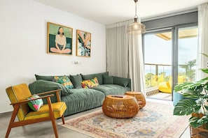Un salón moderno con un sofá verde, un sillón amarillo y un ventanal con vistas.