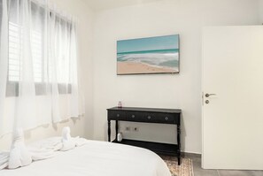 Une chambre d’hôtel avec un lit, un bureau, un tableau représentant une plage et une porte.