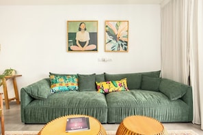 Un sofá verde con cojines coloridos, una mesa de centro de madera y dos cuadros enmarcados en la pared.