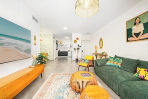 A modern living room with a large flat-screen TV, a green sofa, a wooden coffee table, and a patterned rug.