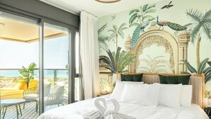 Camera d'albergo con un letto grande, un balcone con sedie gialle e un murale raffigurante uccelli e piante.