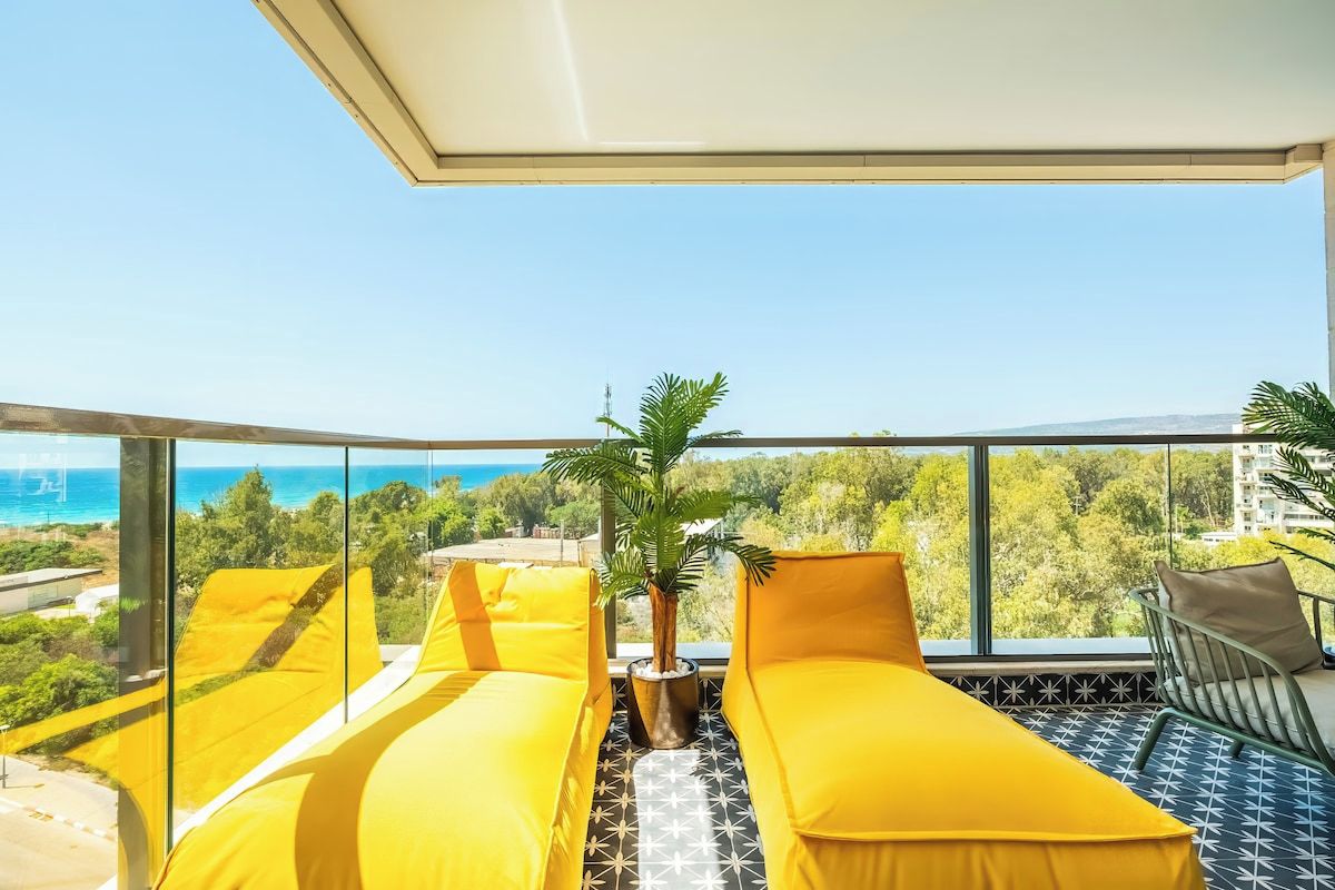 Een balkon met gele zittingen, een klein tafeltje en een potplant.