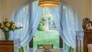 Un coin repas comprenant une table, des chaises, un vase avec des fleurs et une fenêtre avec des rideaux.