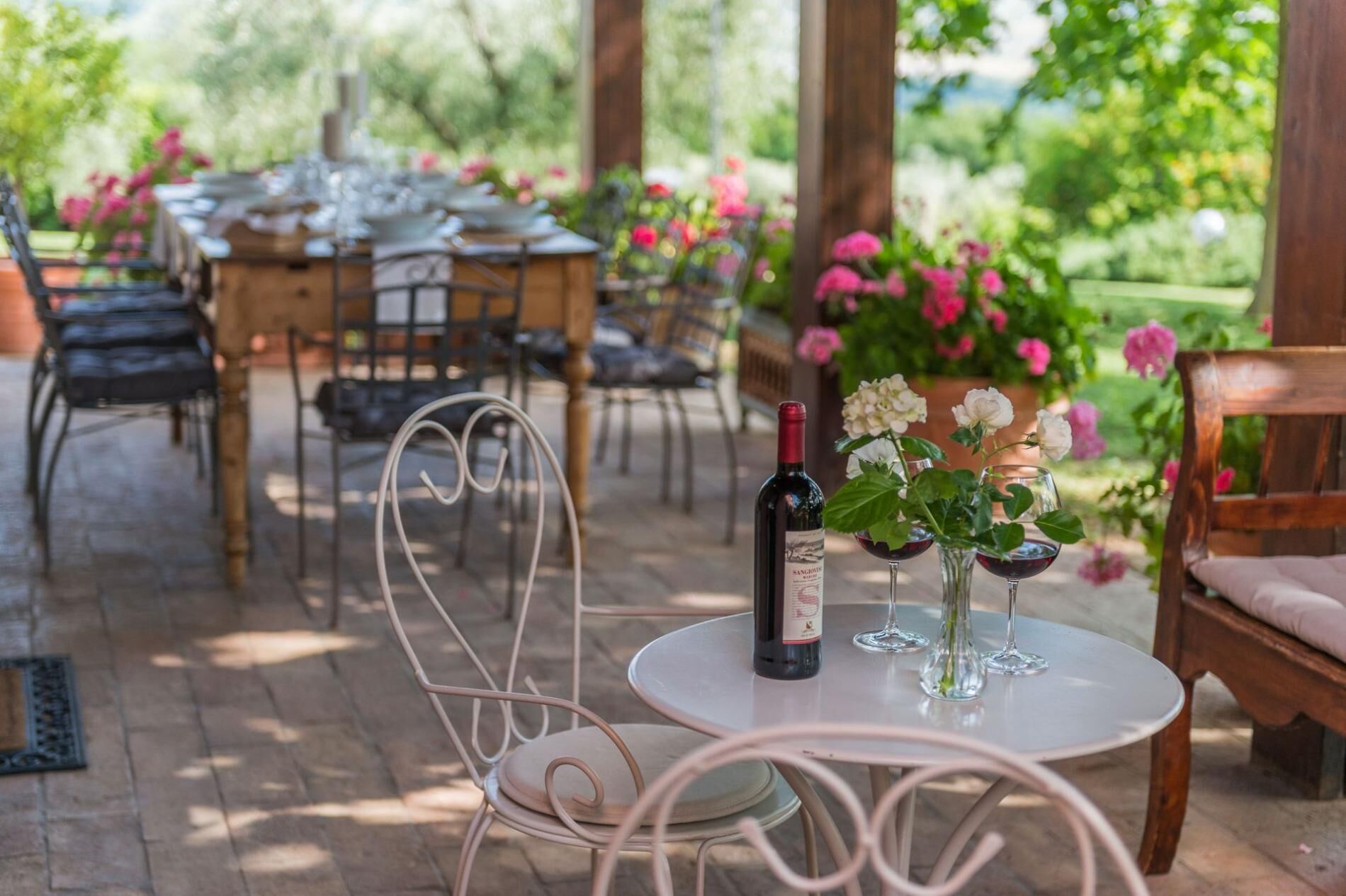 An outdoor dining area with a round table, chairs, and a bottle of wine on a small table.