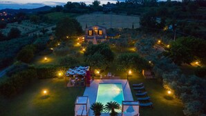 Une grande maison avec une piscine, entourée d’un jardin bien éclairé au crépuscule.