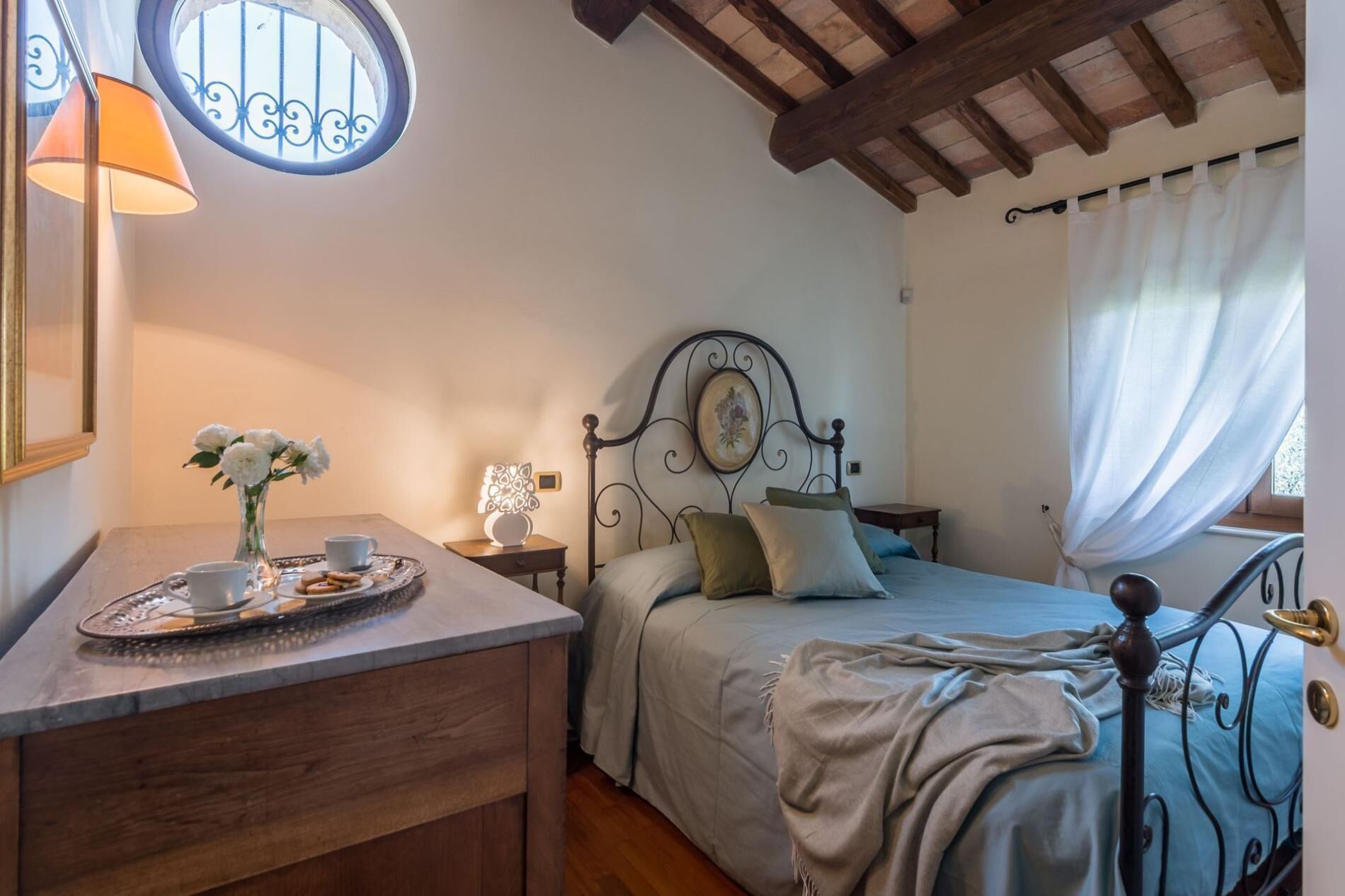 Un dormitorio con cama, una mesita de noche con lámpara, una ventana con cortinas y vistas al exterior.