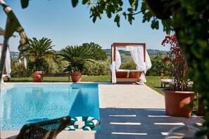 Una piscina con vistas al campo, un espacio de estar techado y plantas en macetas.