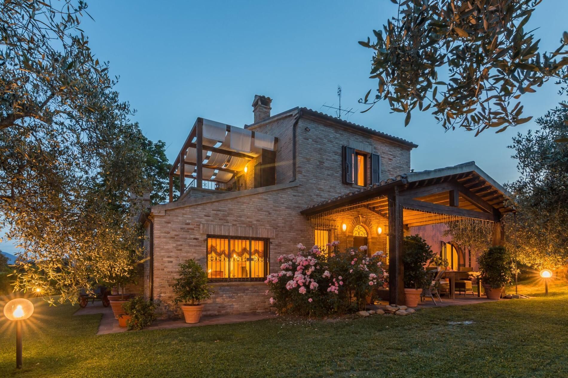 A two-story house with a brick exterior, a covered patio, and a garden with flowering plants.
