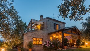 Une maison à deux étages, avec une façade en briques, un patio couvert et un jardin agrémenté de plantes à fleurs.