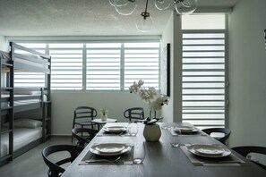 Un comedor con una mesa de madera dispuesta para cuatro personas, sillas alrededor y una ventana con persianas.