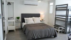 Une chambre à coucher moderne comprenant un lit, des tables de chevet, un ventilateur de plafond, un appareil de climatisation, une lampe de chevet, une plante en pot et une structure de lit superposé.