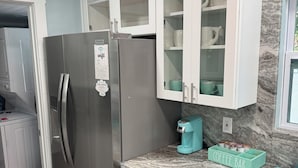 A modern kitchen with white cabinets, a stainless steel refrigerator, a coffee maker, and a marble countertop.