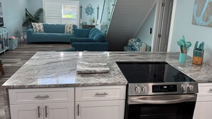 A modern kitchen with a granite countertop, stainless steel appliances, and a dining area with a blue sofa and decorative pillows.