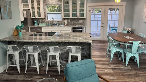 A modern kitchen with white cabinets, a marble countertop, and a dining area with teal chairs.
