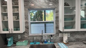A kitchen with marble countertops, white cabinets, and a window with a view of greenery.
