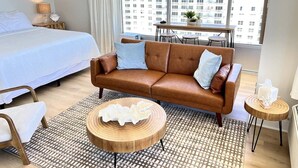 A hotel room with a bed, a brown leather sofa, a round wooden coffee table, and a dining table with chairs. - Beachfront & Oceanfront Views – Private Balcony (Daytona Beach)