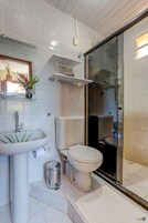 Un baño moderno con lavamanos blanco, inodoro y ducha con mampara de vidrio.