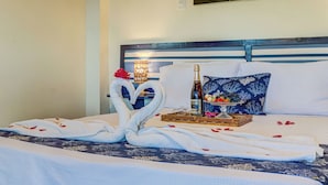 Una cama bien hecha con un arreglo decorativo de toallas, una botella y una bandeja de fruta.