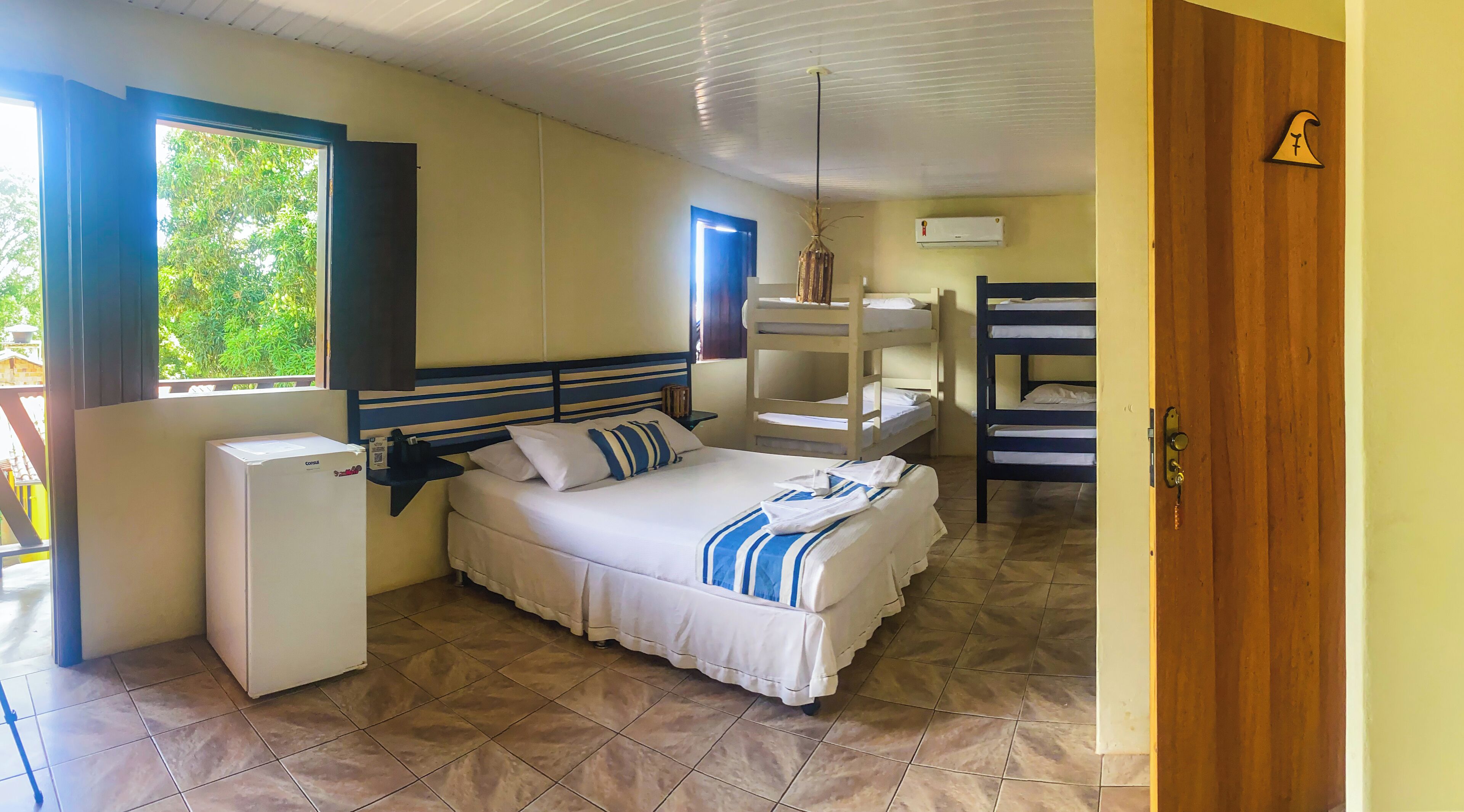Quarto com cama, pequeno frigorífico, janela e beliche.