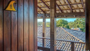 Una puerta de madera con un cartel de número, una barandilla metálica y vistas a un tejado con tejas y follaje.