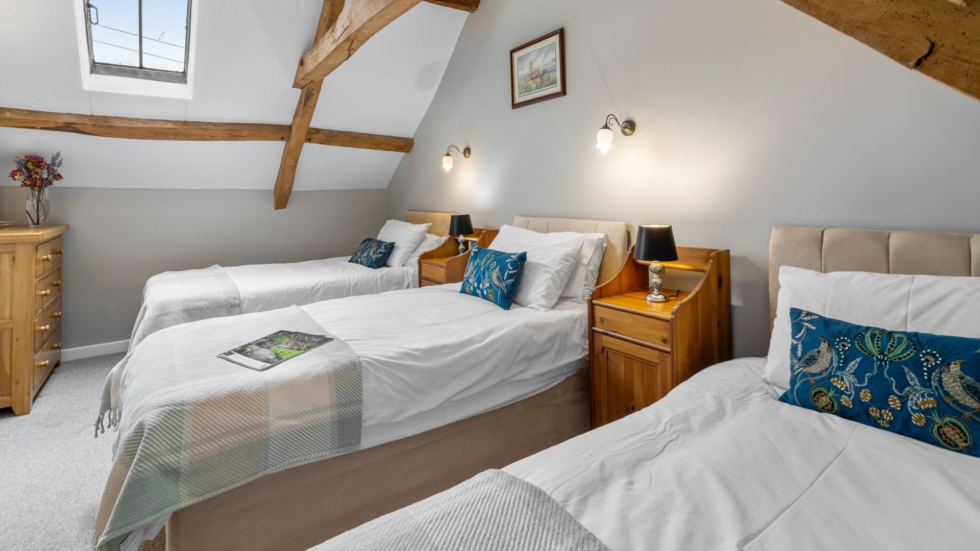A room with two single beds, wooden headboards, a wooden dresser, and a window with a view.