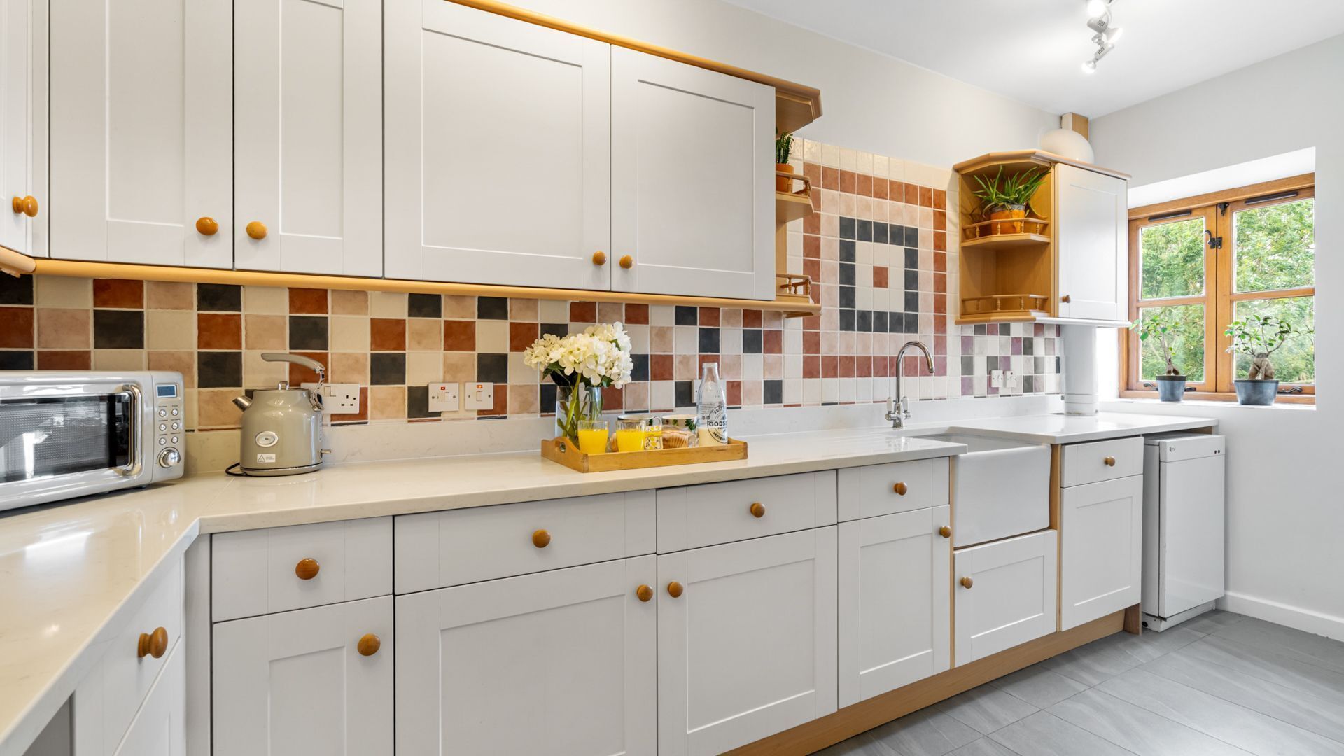 A modern kitchen with white cabinets, a microwave, a kettle, and a breakfast tray on the counter.